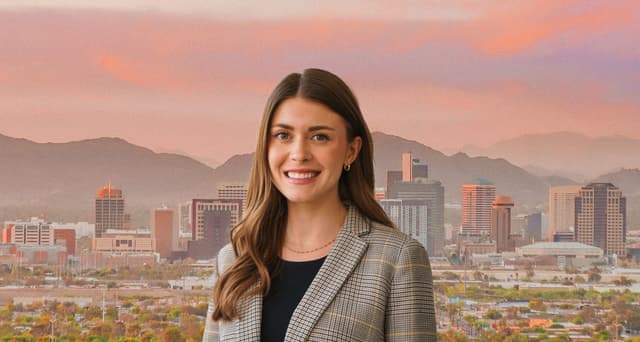 Natalie Storm, Director of Property Marketing smiles in front of the Phoenix skyline at sunset, with soft pink and orange hues over the mountains in the background for Bisnow Women Leading Award